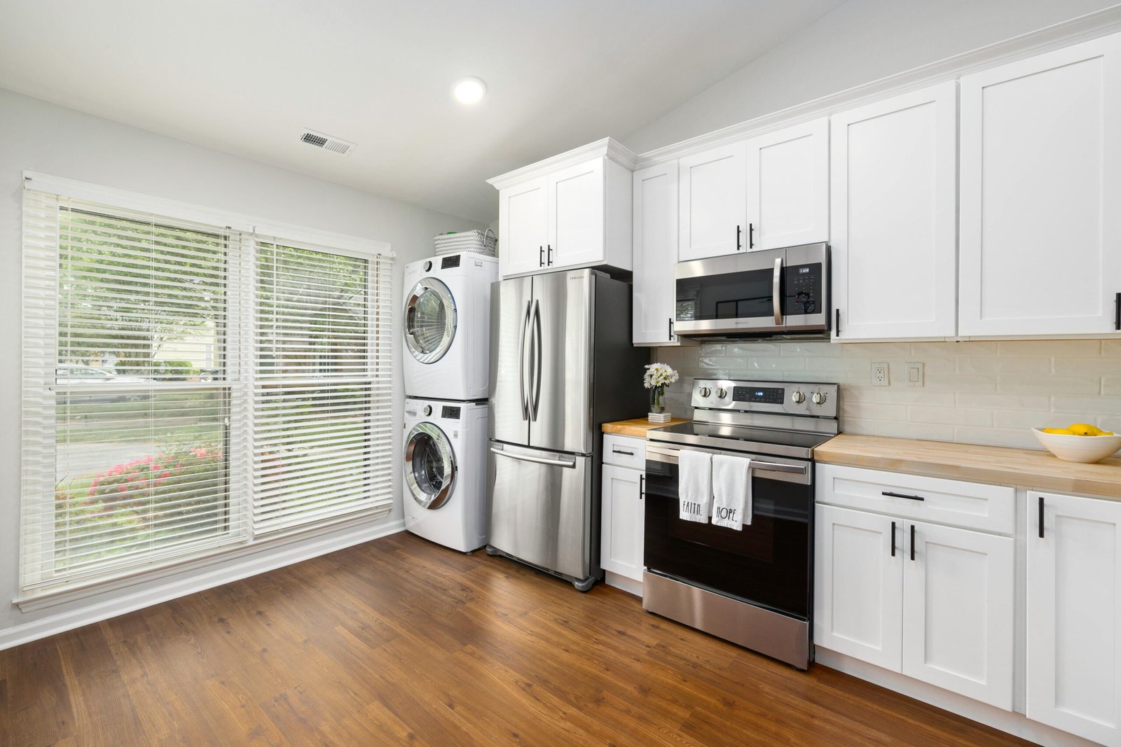 A modern kitchen featuring stainless steel appliances, white cabinets, and a wooden floor with ample natural light.